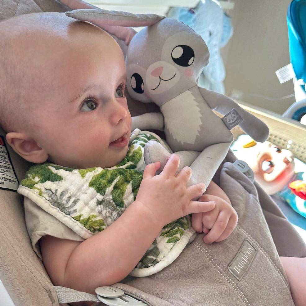 paris hiltons baby sitting in a babybjorn bouncer seat holding a bunny rabbit doll
