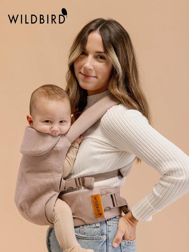 a woman carrying a baby in the leopard print wildbird aerial baby carrier